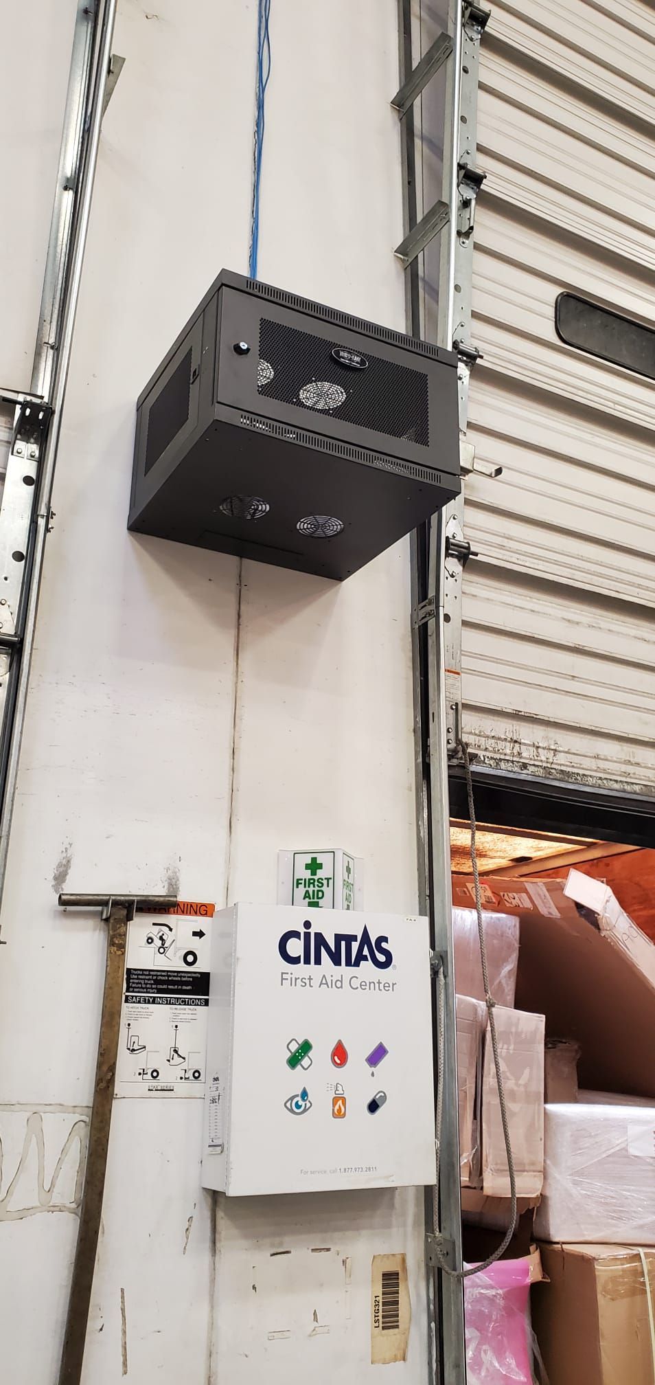 Gray box on a wall, below is a Cintas box with icons. The wall is near a garage door.