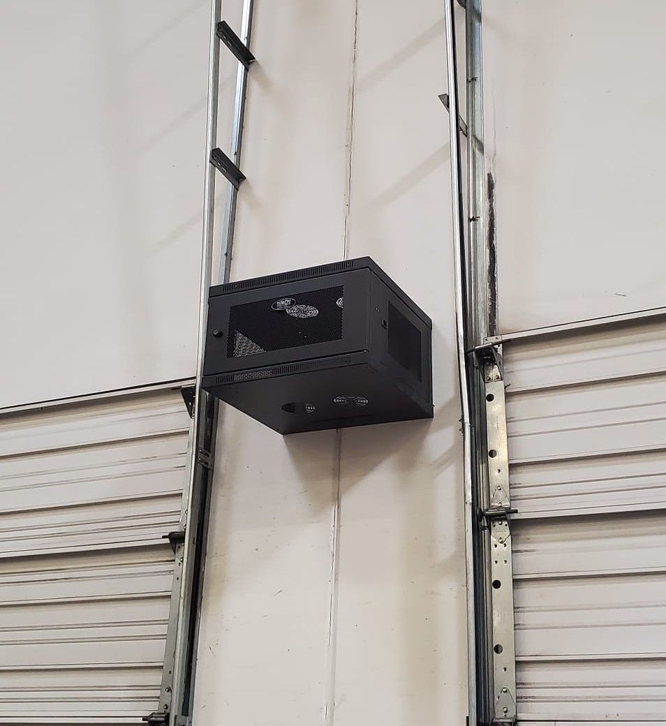Black metal server rack mounted on a white wall next to a metal ladder and siding.