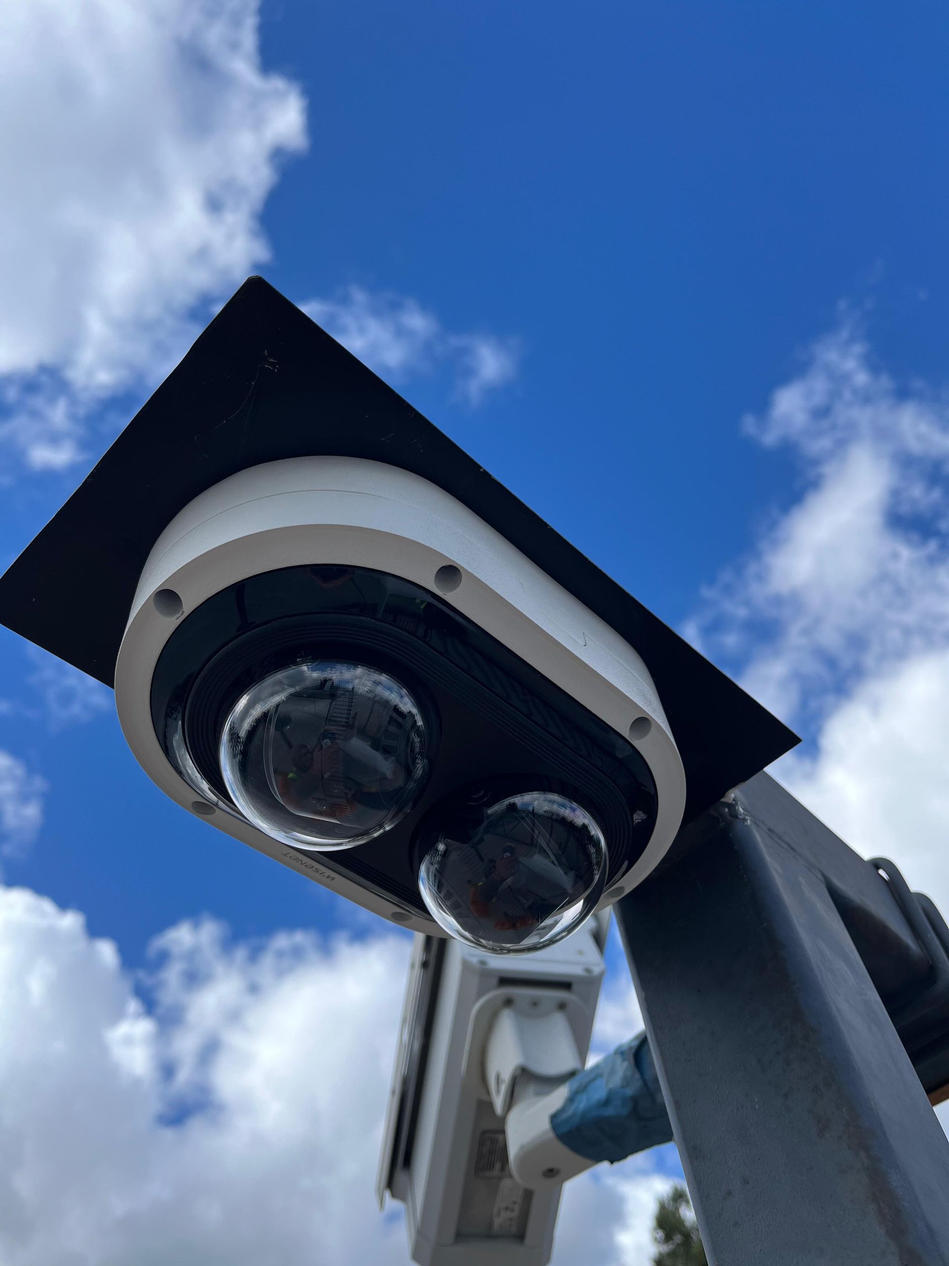 Security camera with two rounded lenses, mounted outdoors against a cloudy blue sky.