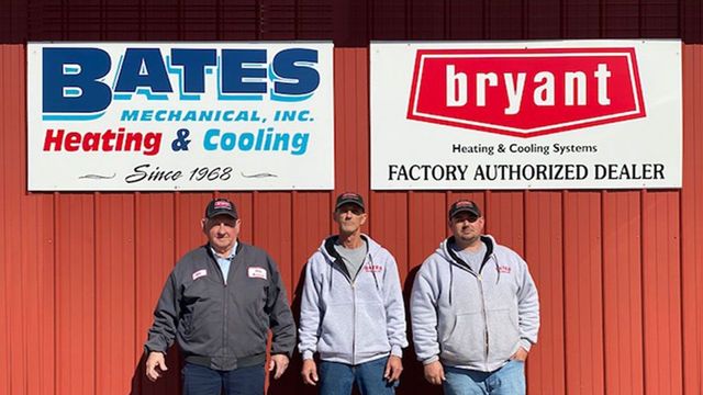 Three men are standing in front of a sign for bates mechanical inc.