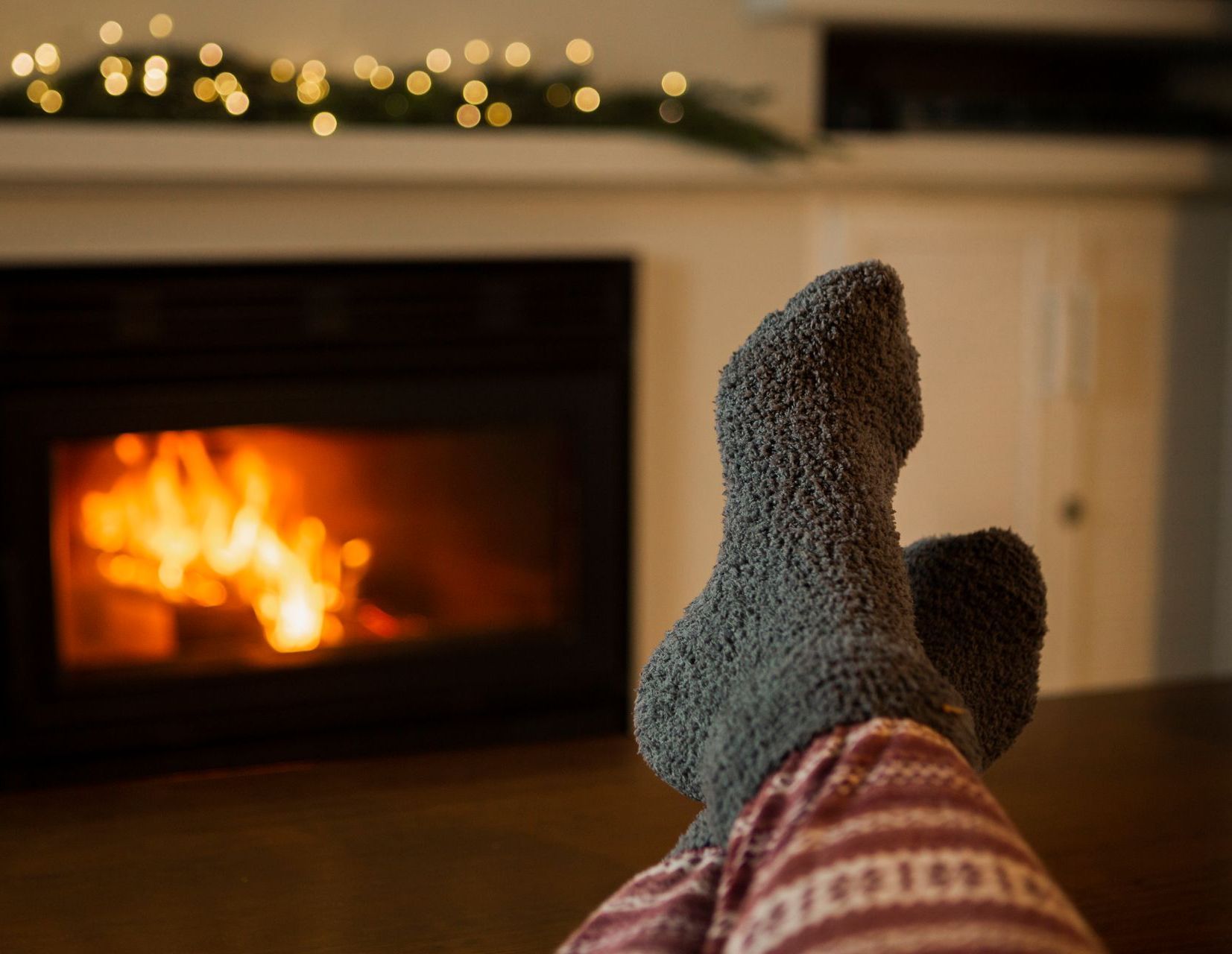 A person is laying on a couch with their feet up in front of a fireplace.