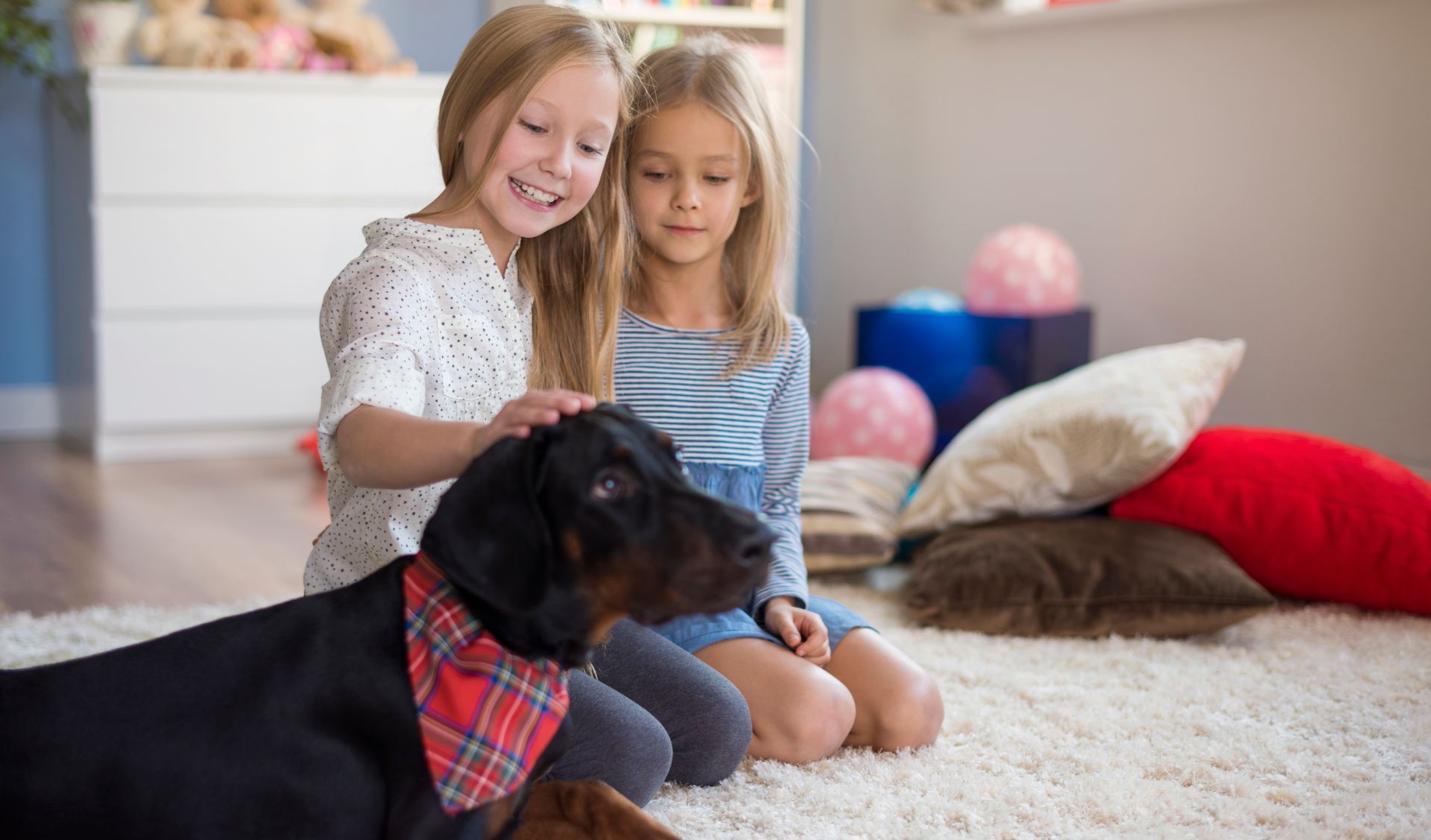 Two little girls are petting a dog while sitting on the floor.