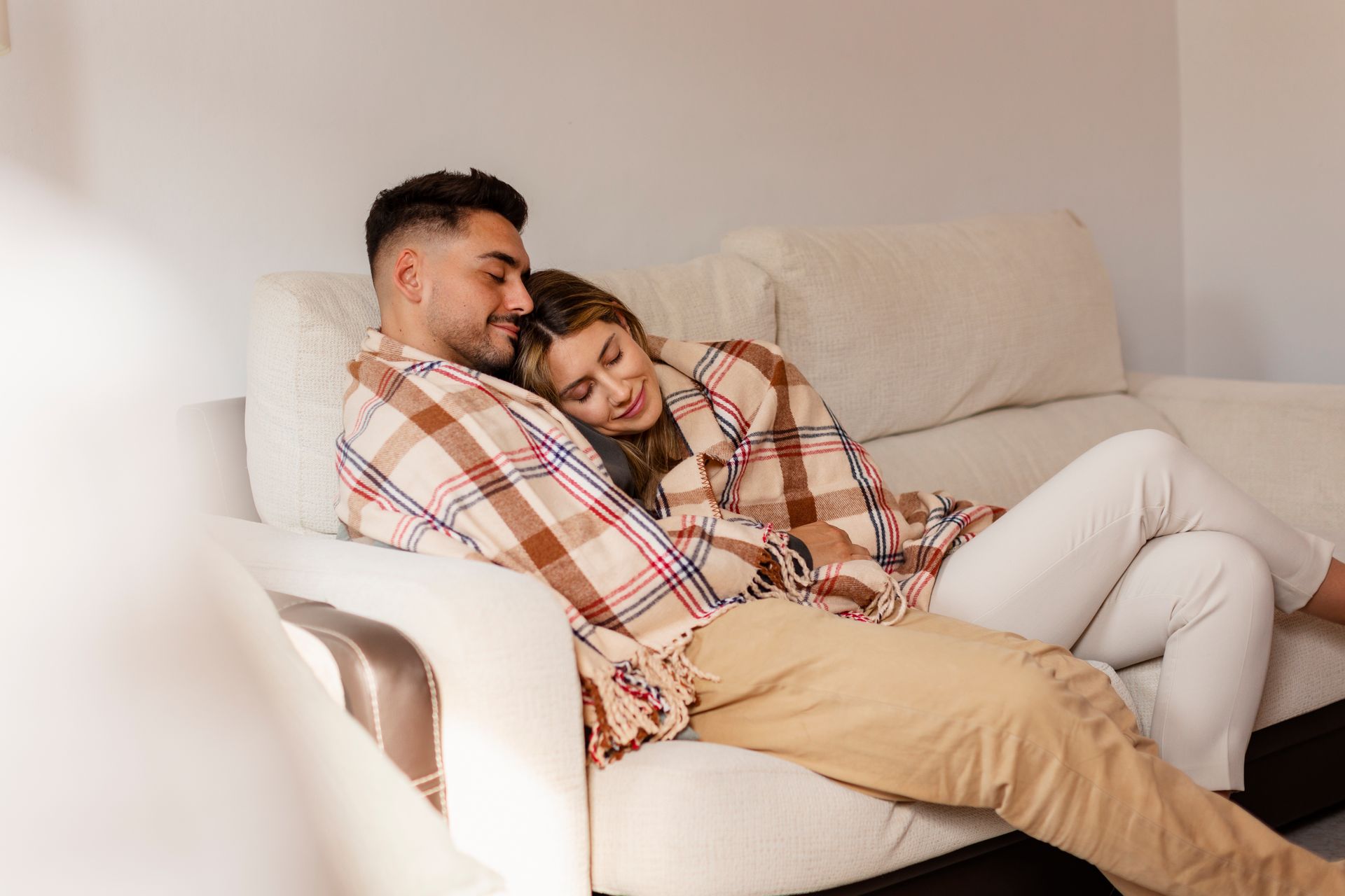 A man and a woman are laying on a couch under a blanket.