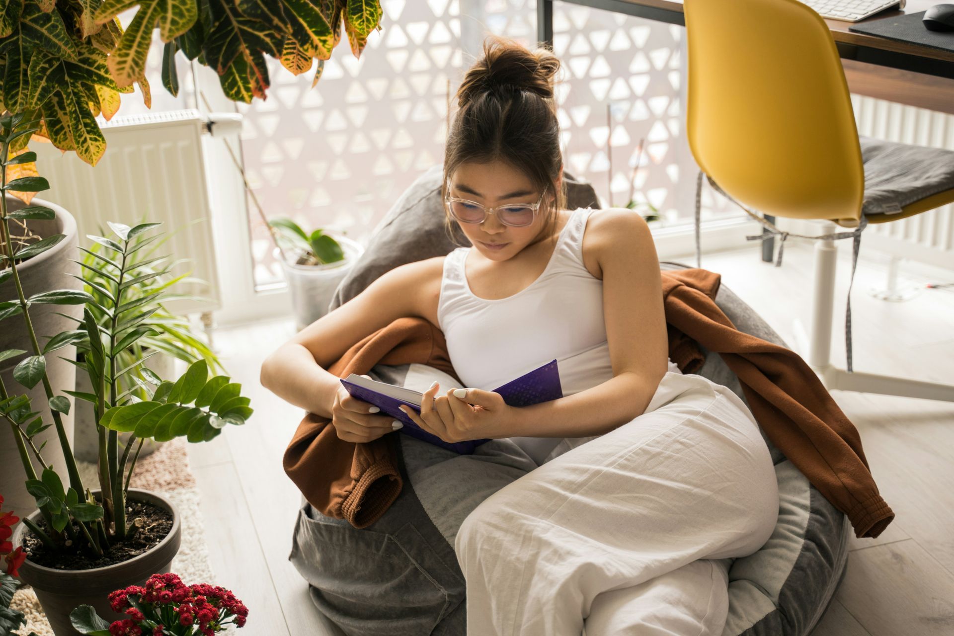 A woman is sitting on a bean bag chair reading a book.