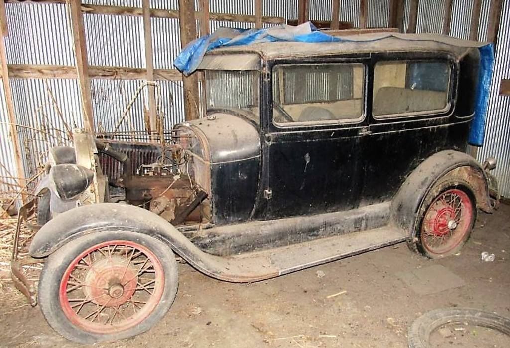 Old black vintage car with red wheels parked inside a rustic shed