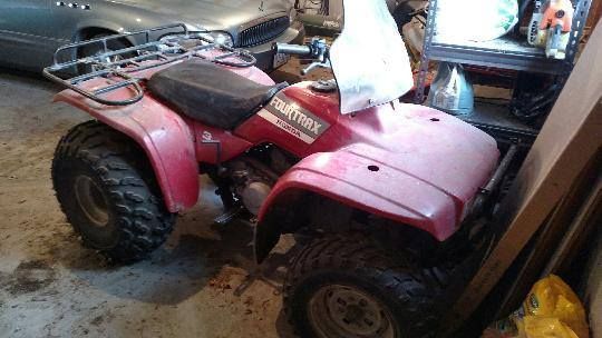 Red ATV parked in a garage beside a silver car, with a white bag on the seat.