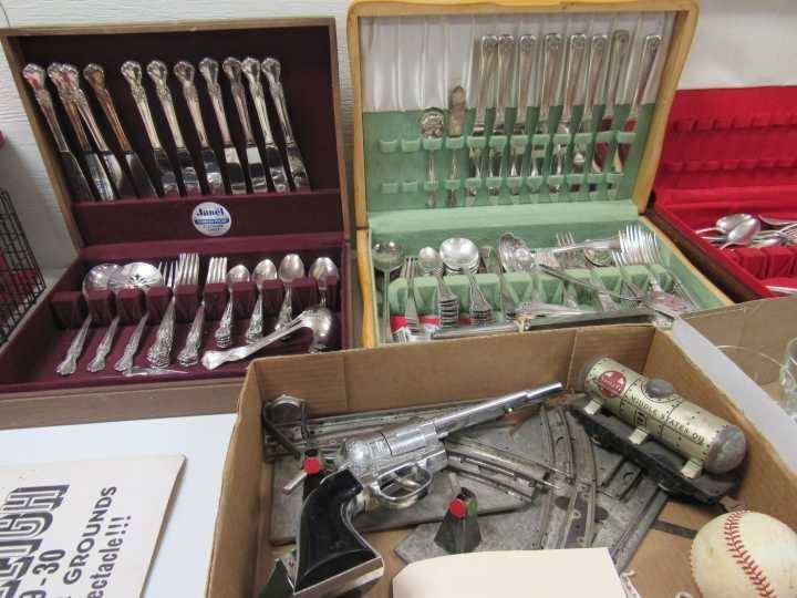 Assorted silverware and utensils displayed in open cases and boxes at a flea market table