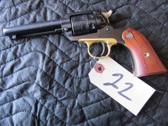 Black revolver with wooden grip and a white “22” tag on a quilted surface