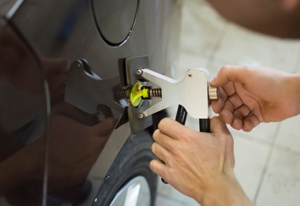 Hands Using a Dent Repair Tool on a Car's Black Body Panel, Next to a Tire — Bob Kolln Automotive In Warnervale, NSW