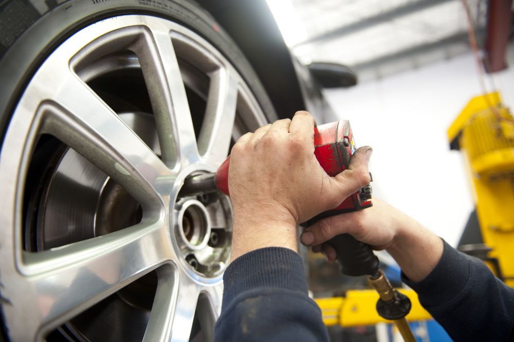 Hands Using a Red Power Tool to Remove a Tire From a Car's Wheel in a Garage — Bob Kolln Automotive In Woongarrah, NSW