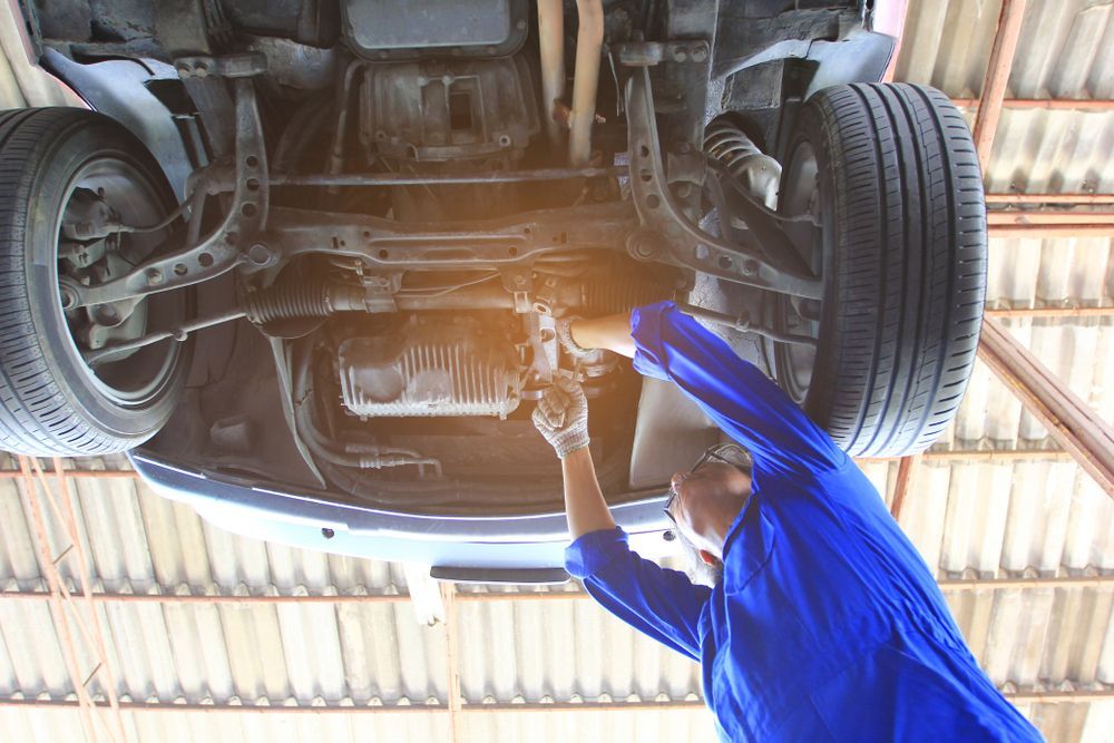 Mechanic in Blue Jumpsuit Working Under a Car on a Lift in a Garage — Bob Kolln Automotive In Charmhaven, NSW