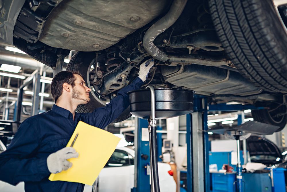 Mechanic in Blue Uniform Inspects Undercarriage of Car on a Lift — Bob Kolln Automotive In Charmhaven, NSW
