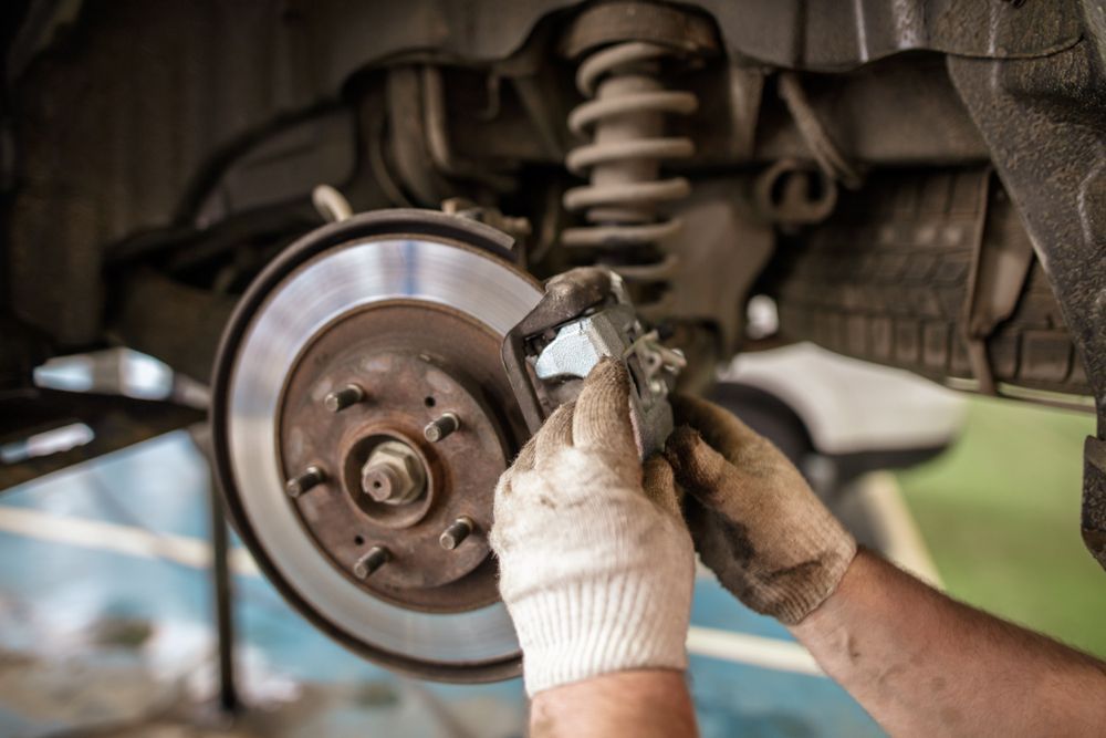 Person Wearing Gloves Replacing Brake Pads on a Car's Brake Disc in a Garage — Bob Kolln Automotive In Charmhaven, NSW