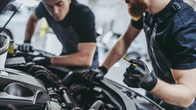 Two mechanics inspecting a car engine, one holding a diagnostic tool in a garage