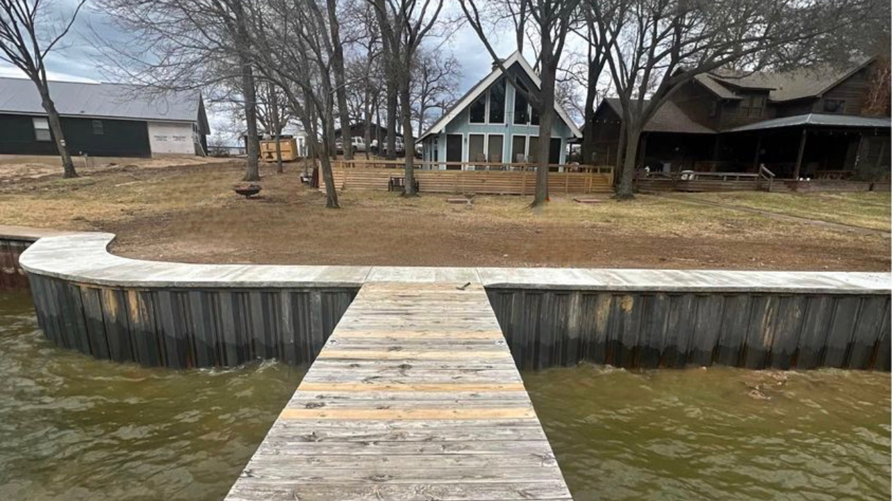 A wooden dock leading to a house on a lake.