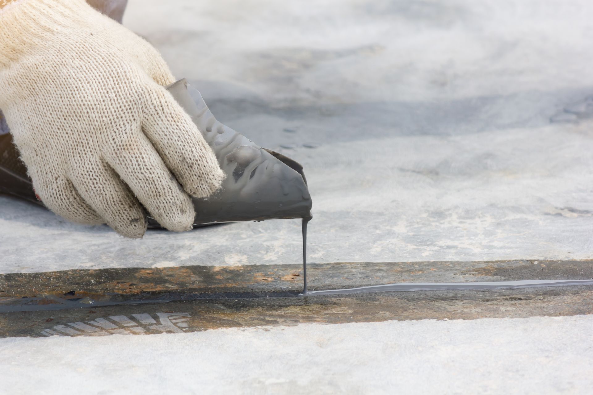 A person is applying a rubber seal to a concrete surface.
