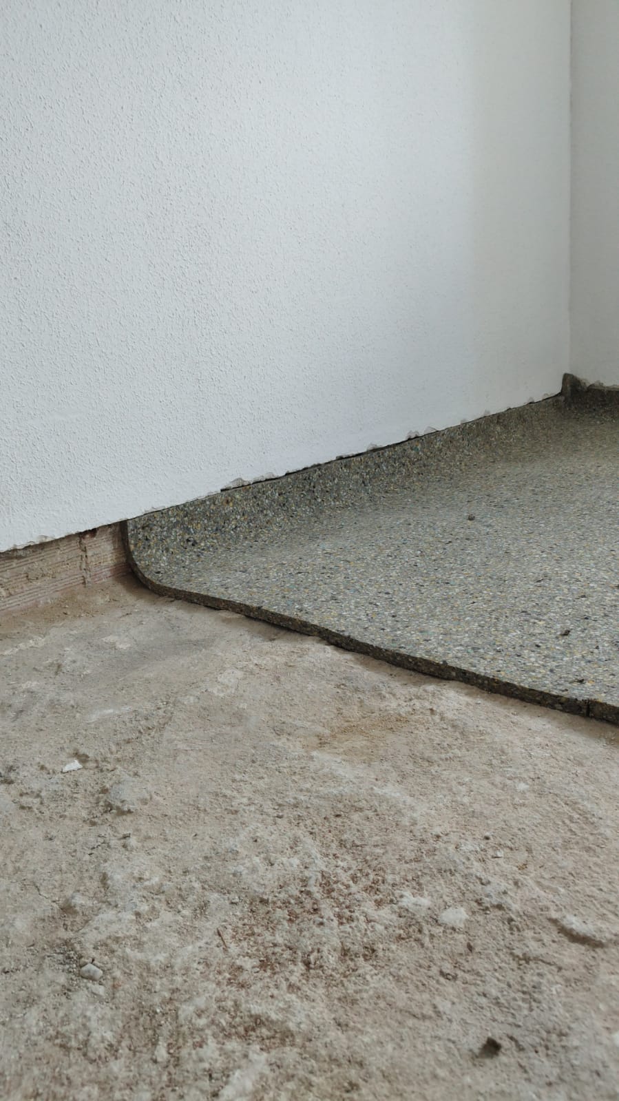 Una habitación con piso de concreto y una pared blanca.