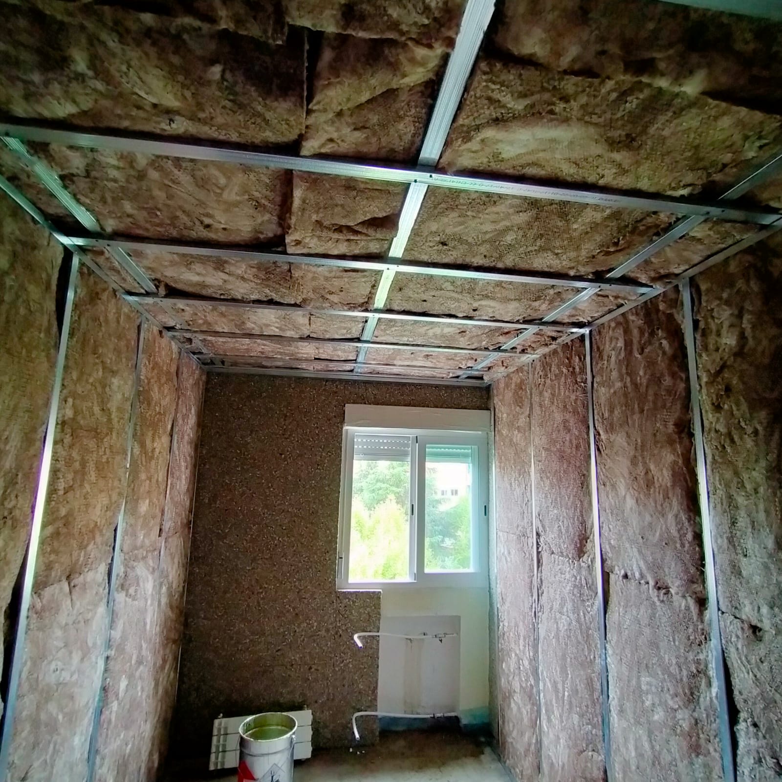 Una habitación con una ventana y un cubo en el suelo