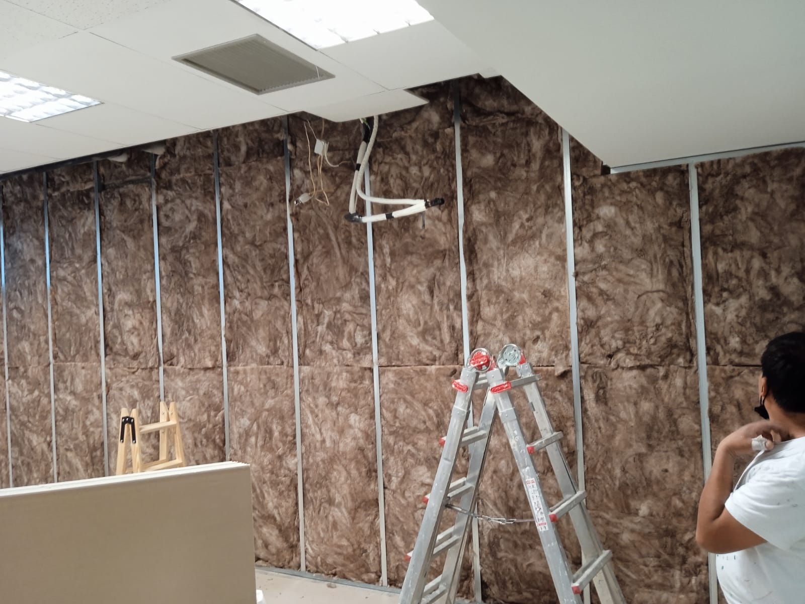 Un hombre está parado frente a una pared con aislamiento y una escalera.