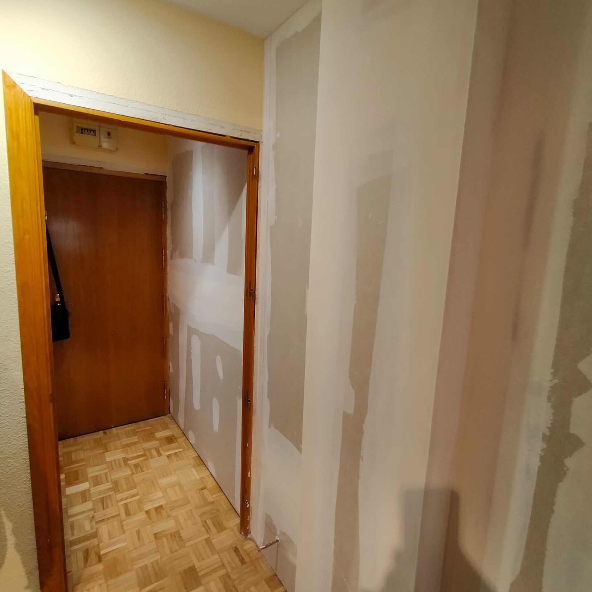 Un pasillo con puerta de madera y pared blanca.