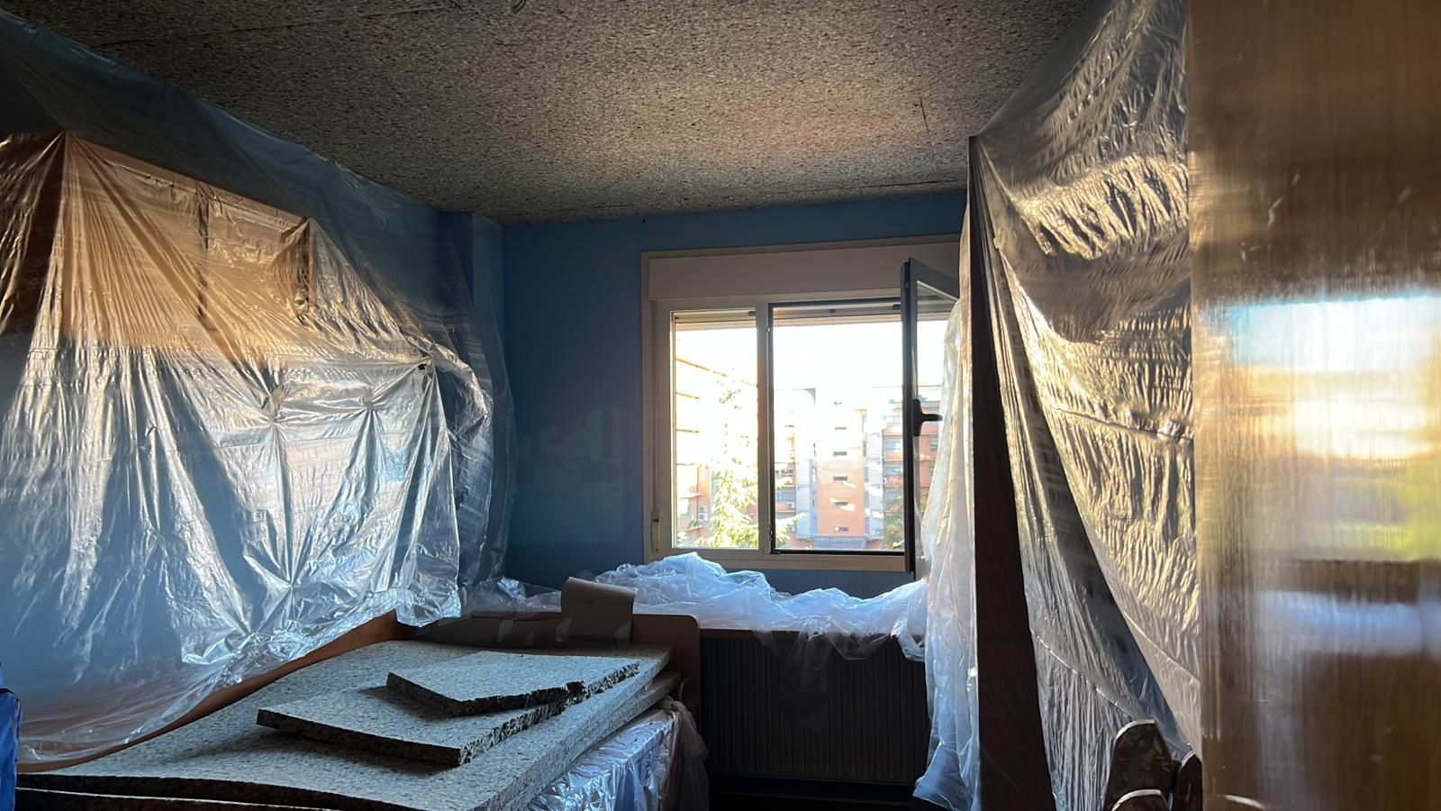 Una habitación con una cama y una ventana revestida de plástico.