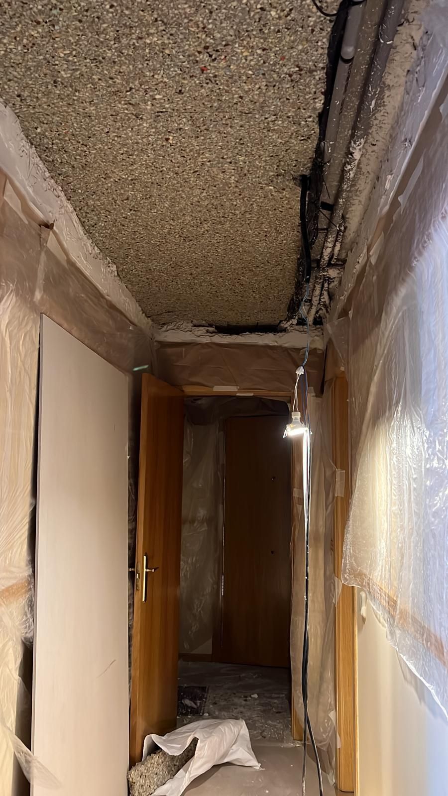 Un largo pasillo con puerta y techo que está siendo remodelado.