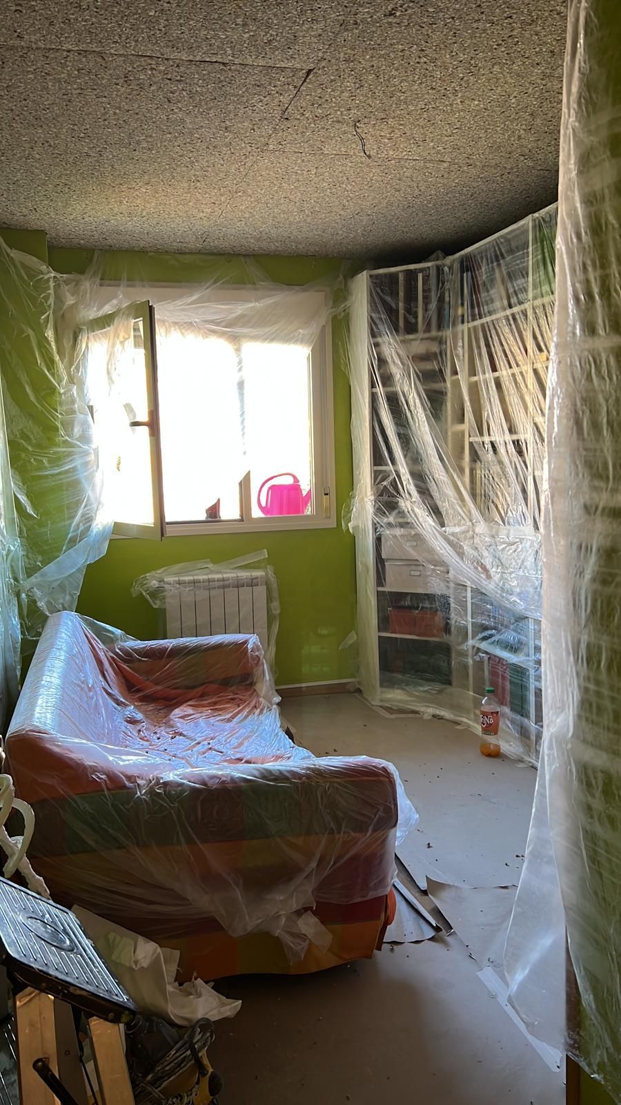 Una habitación con un sofá envuelto en plástico y una ventana.