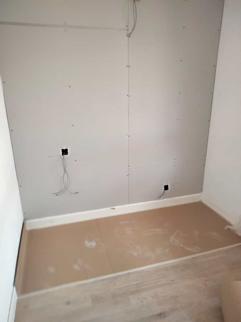 Una habitación vacía con suelo de madera y una pared blanca.