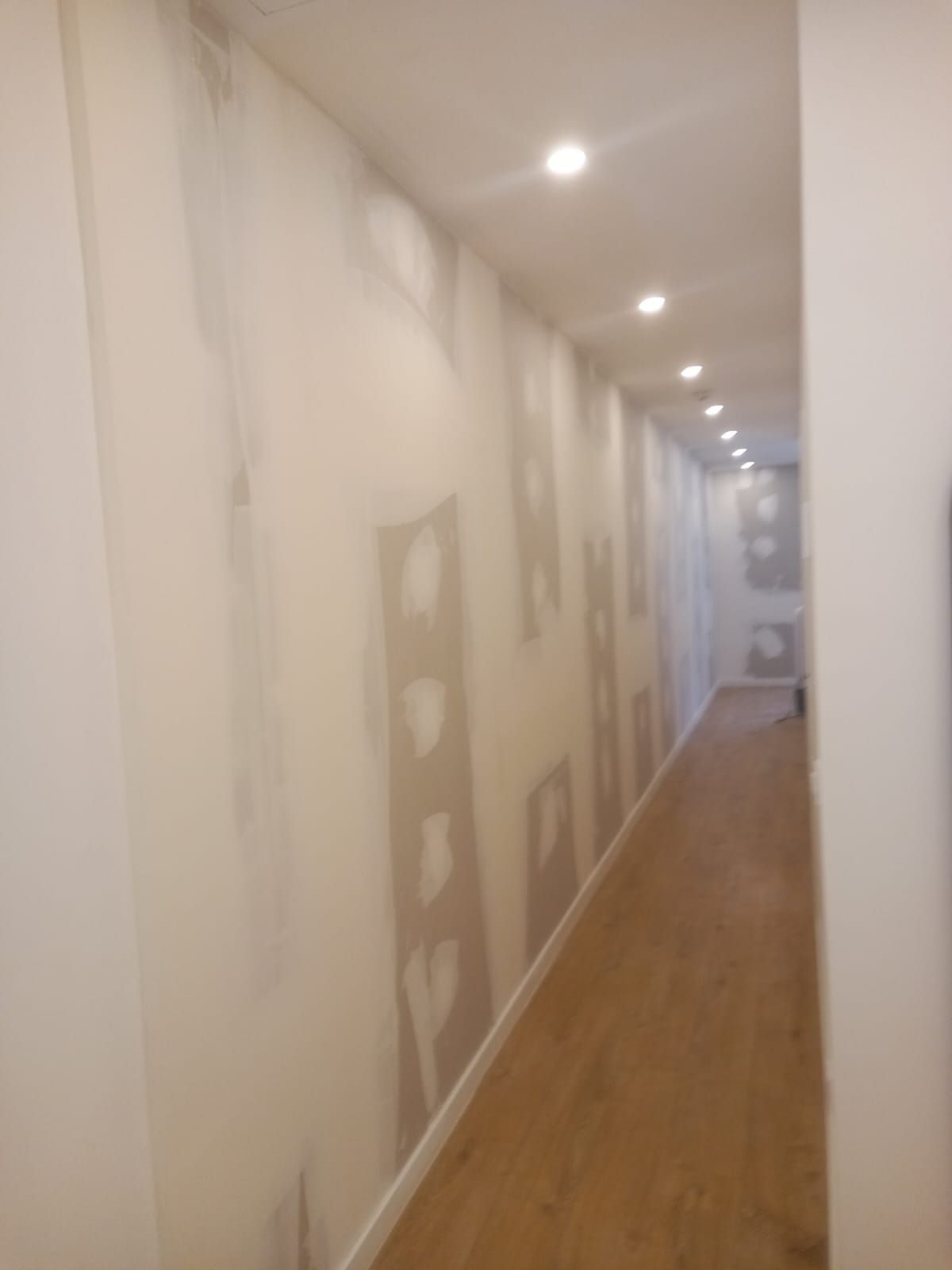 Un pasillo largo con suelo de madera y paredes blancas.