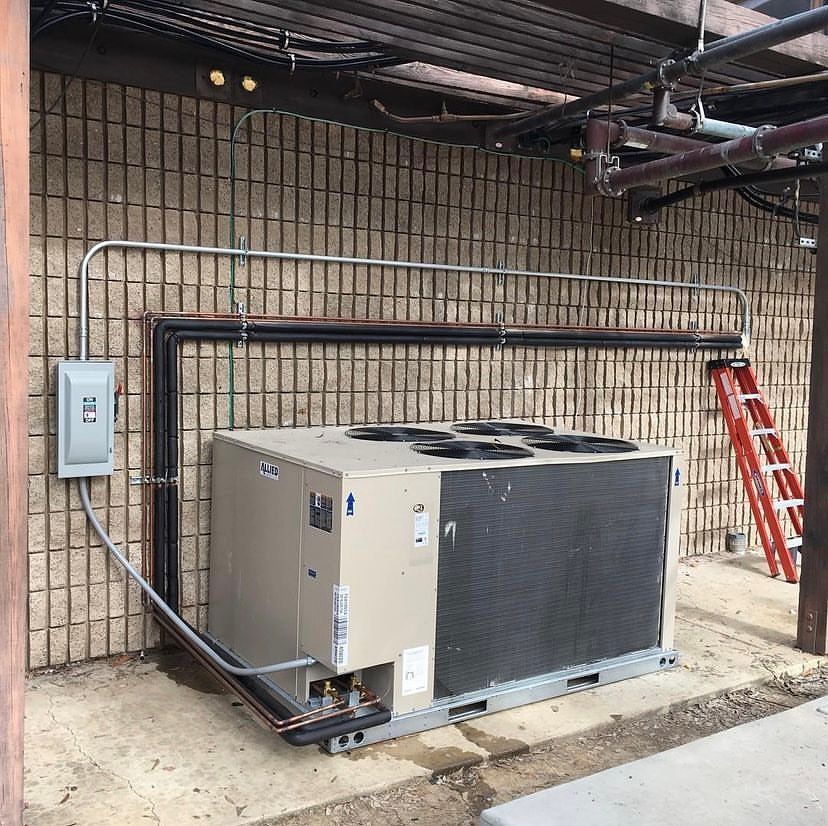 A large air conditioner is sitting in front of a brick wall.