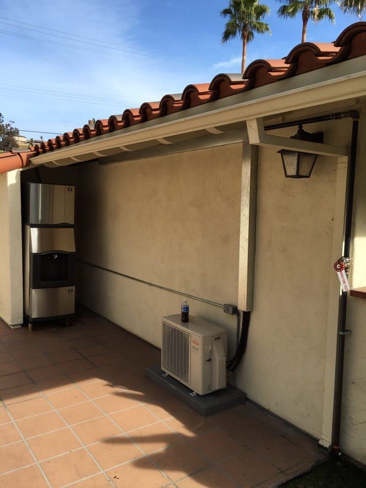 A stainless steel refrigerator is sitting under a roof.
