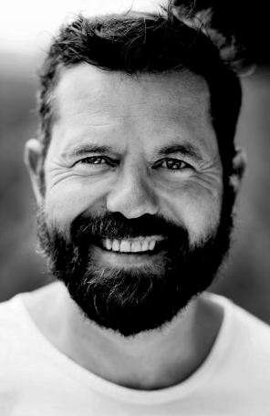 A man with a beard is smiling in a black and white photo.