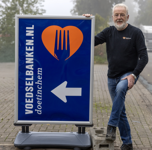 A man standing next to a sign that says voedselbanken.nl