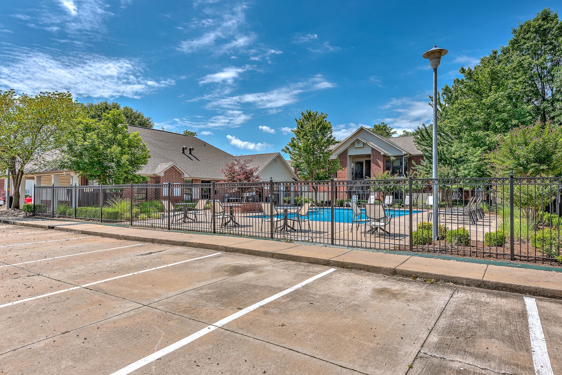 A parking lot in front of a house with a pool in the background.