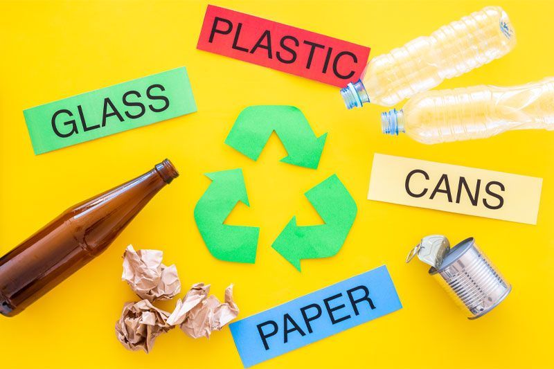 A recycling symbol is surrounded by bottles , cans , paper and glass.