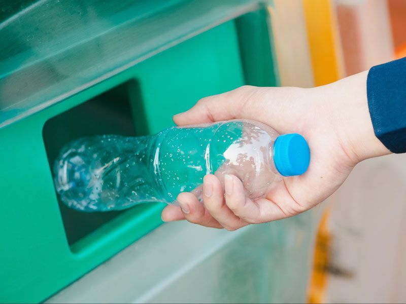 A person is putting a plastic bottle into a recycling bin.