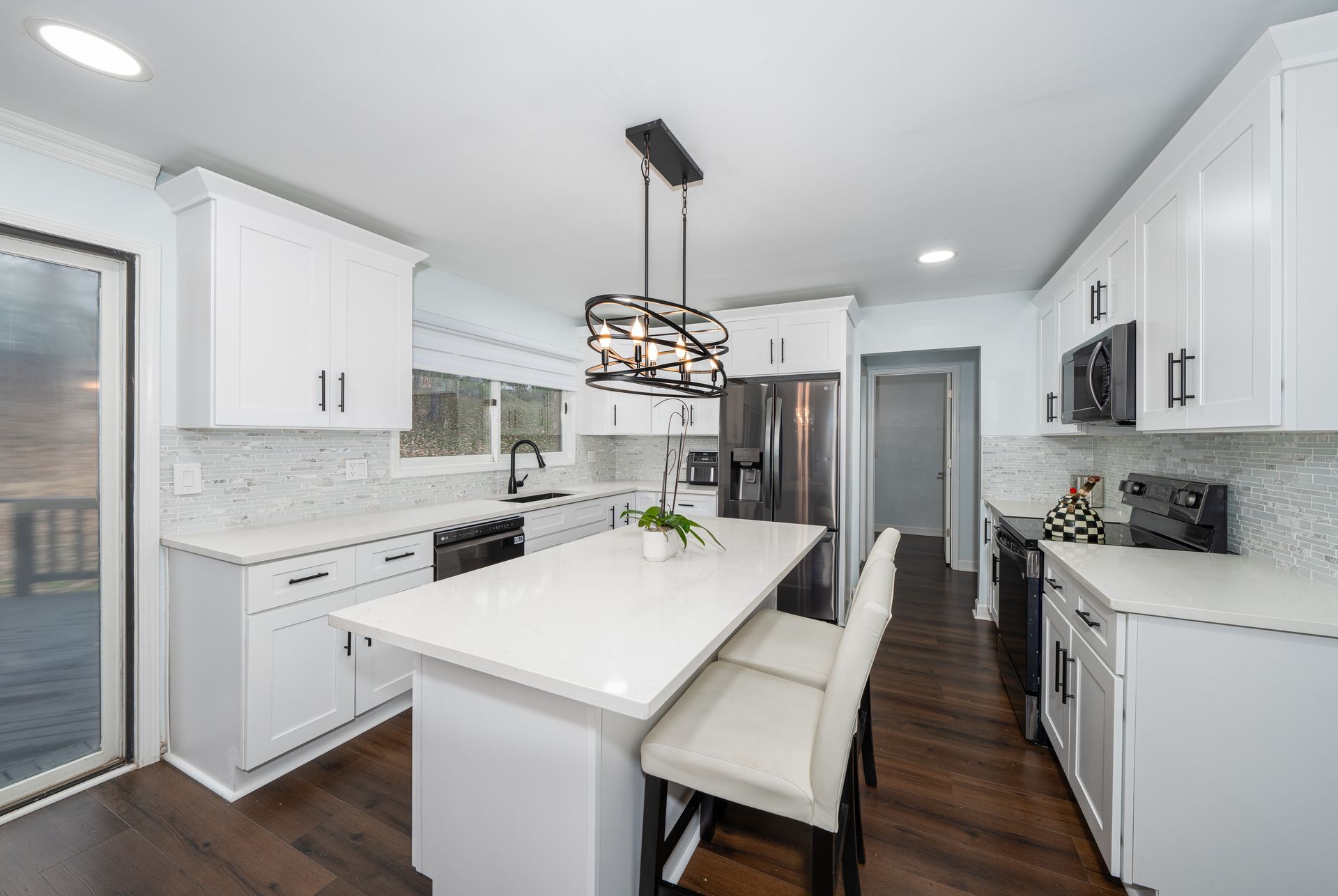 Bright modern white kitchen with island, pendant light, stainless appliances, and dark wood floors.