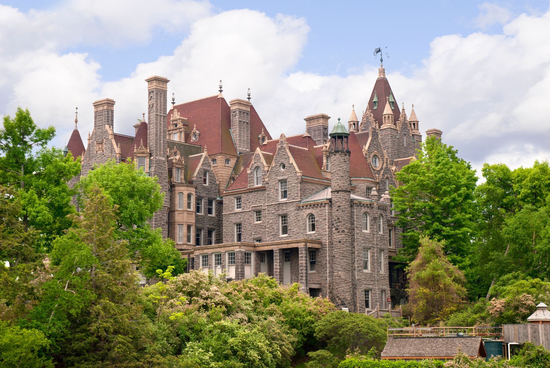 A large stone building with a red roof is surrounded by trees