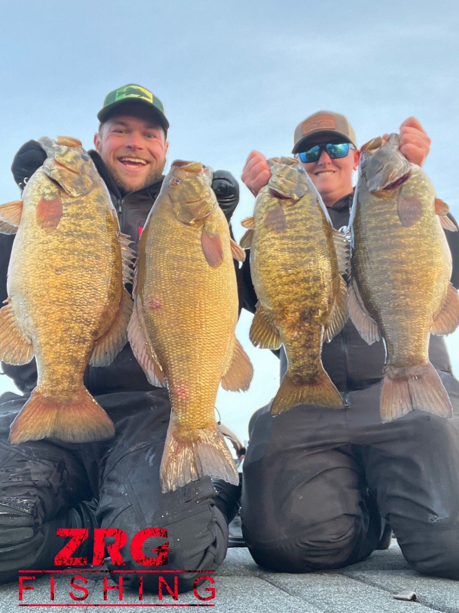 Two men are kneeling down holding three large fish.