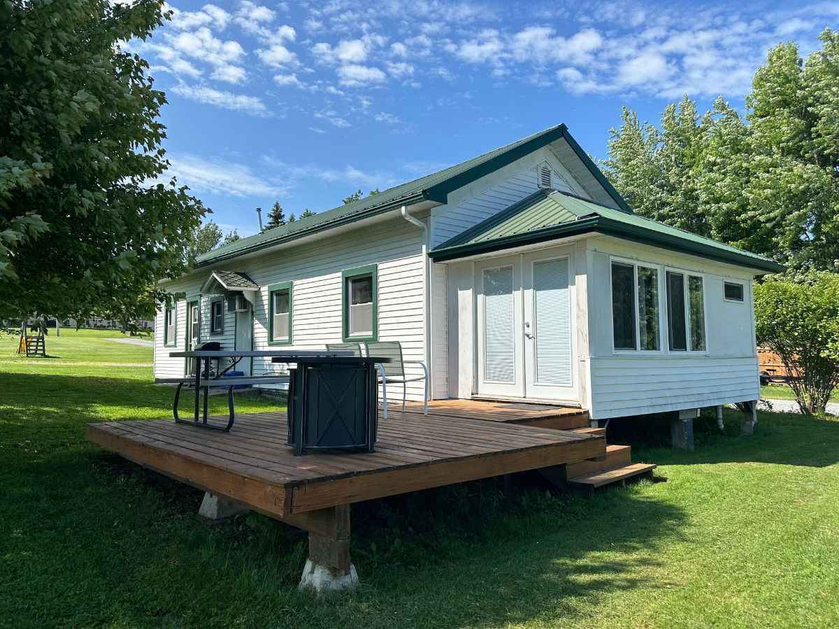 A small white house with a green roof and a picnic table on the deck.