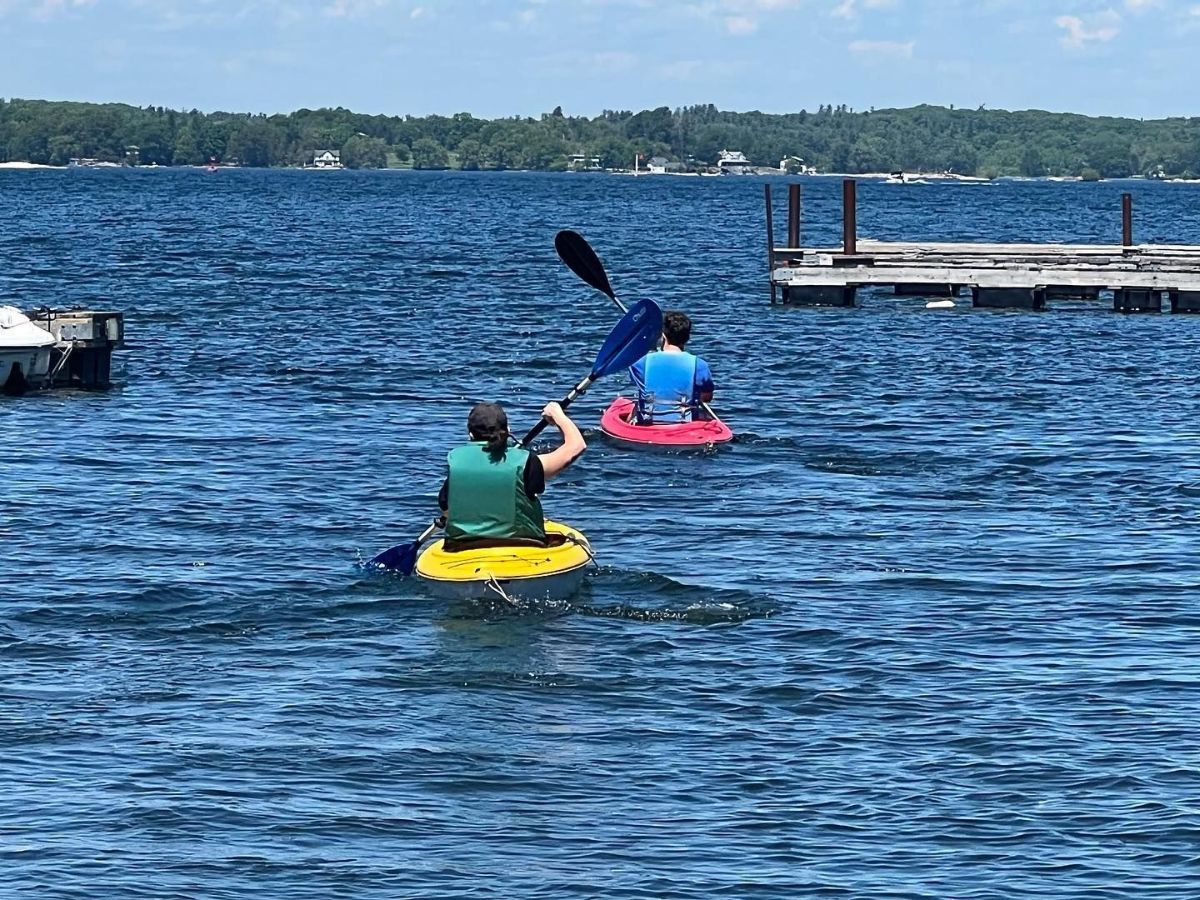 Two people are kayaking on a lake near a dock.