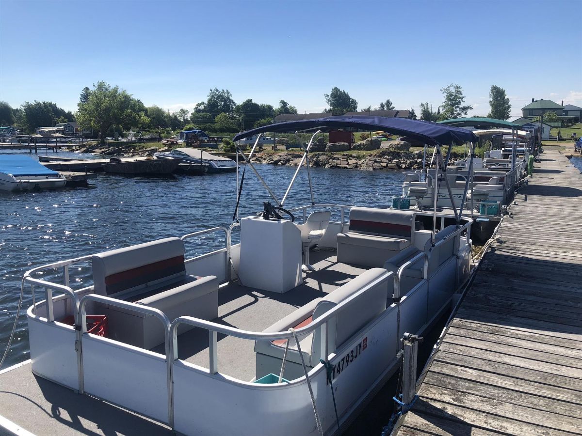 A row of pontoon boats are docked at a dock.