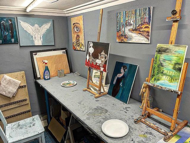 Uno studio di pittura con un tavolo, cavalletti e quadri alle pareti.