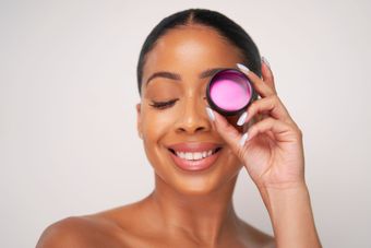 A woman is holding a pink container in front of her eye.