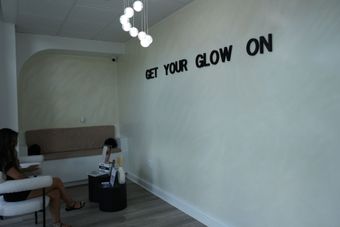 A woman sits in a chair in front of a wall that says get your glow on