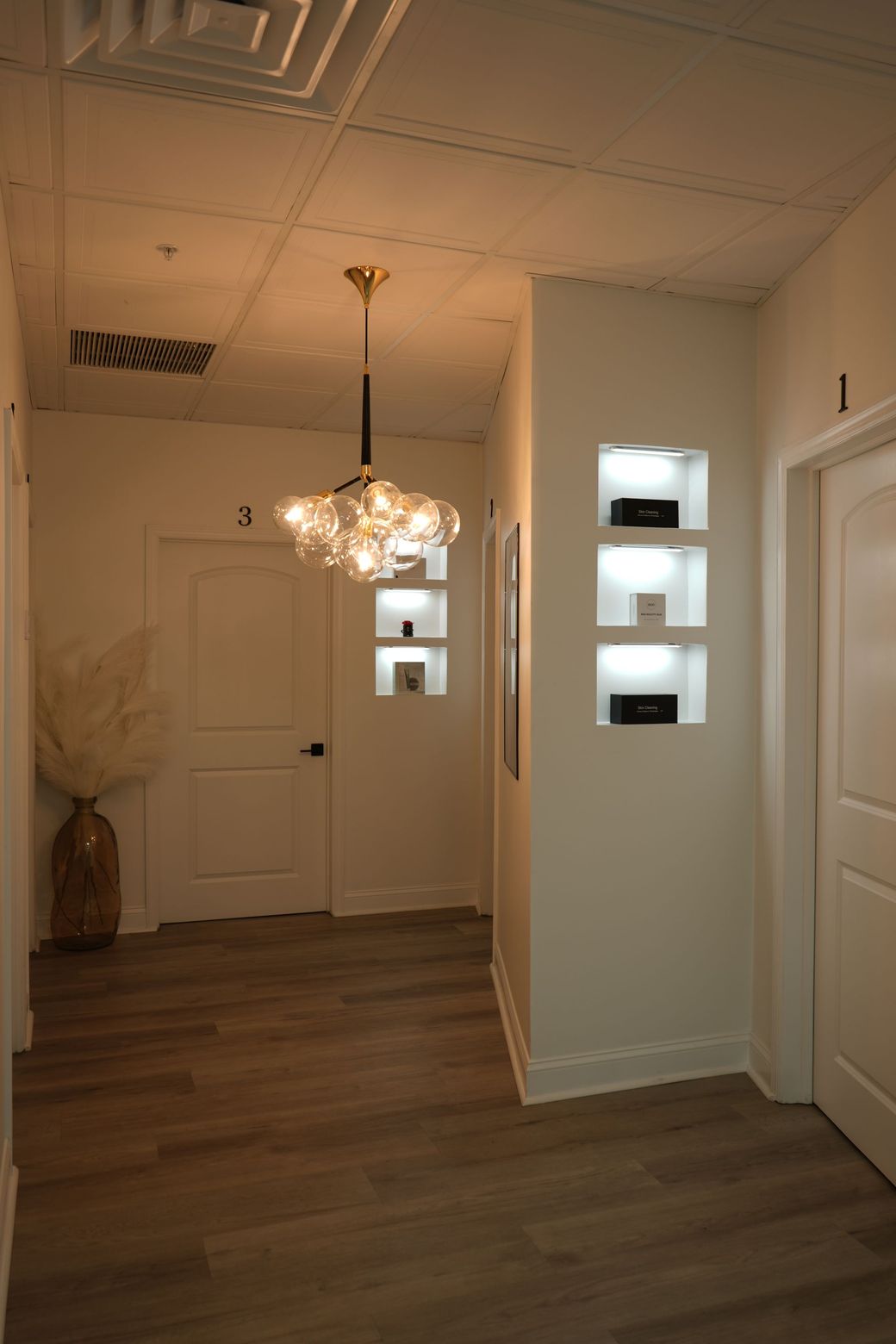 A hallway with a chandelier hanging from the ceiling and shelves on the wall.