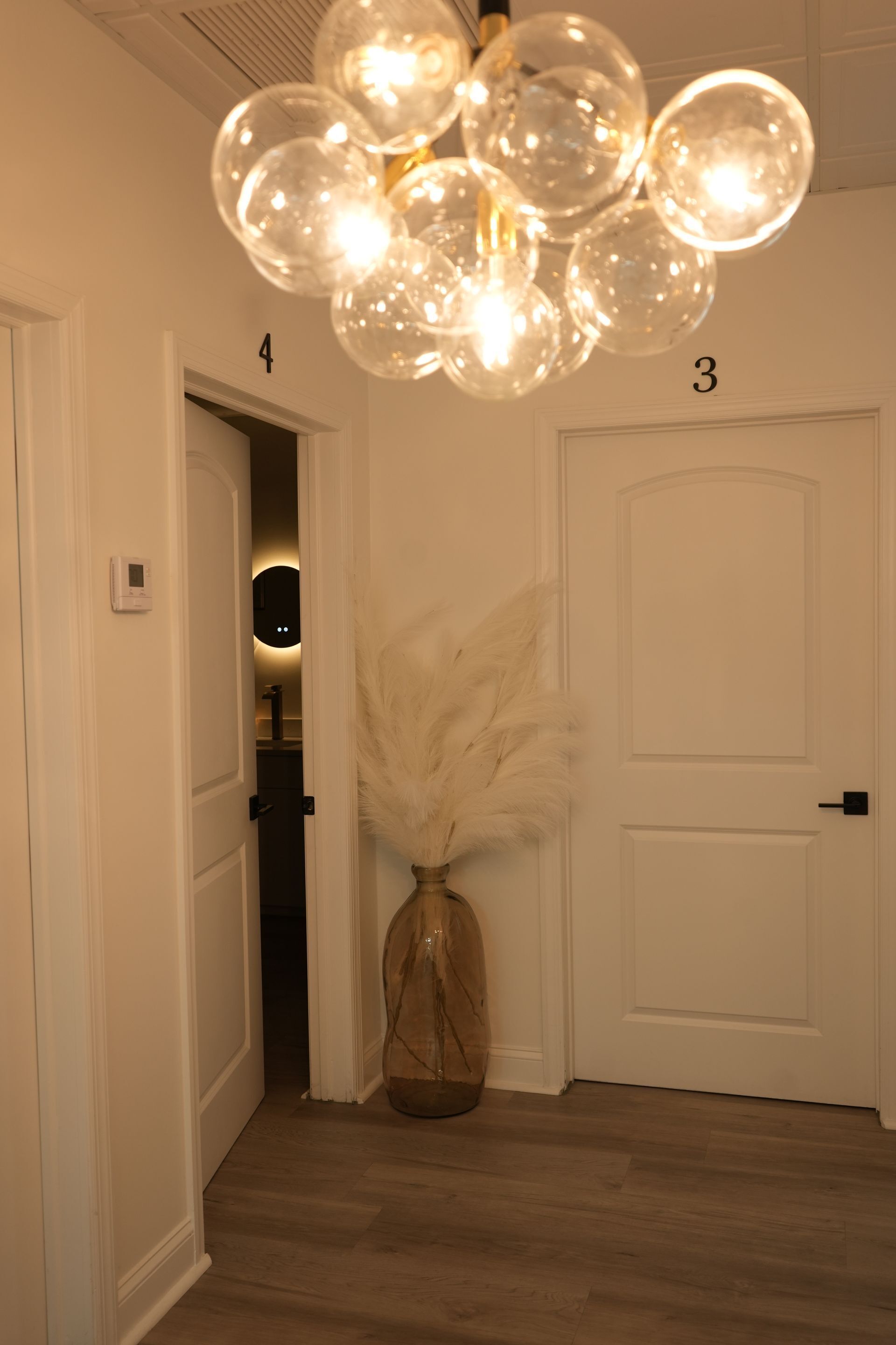 A hallway with a vase of pampas grass and a chandelier hanging from the ceiling.