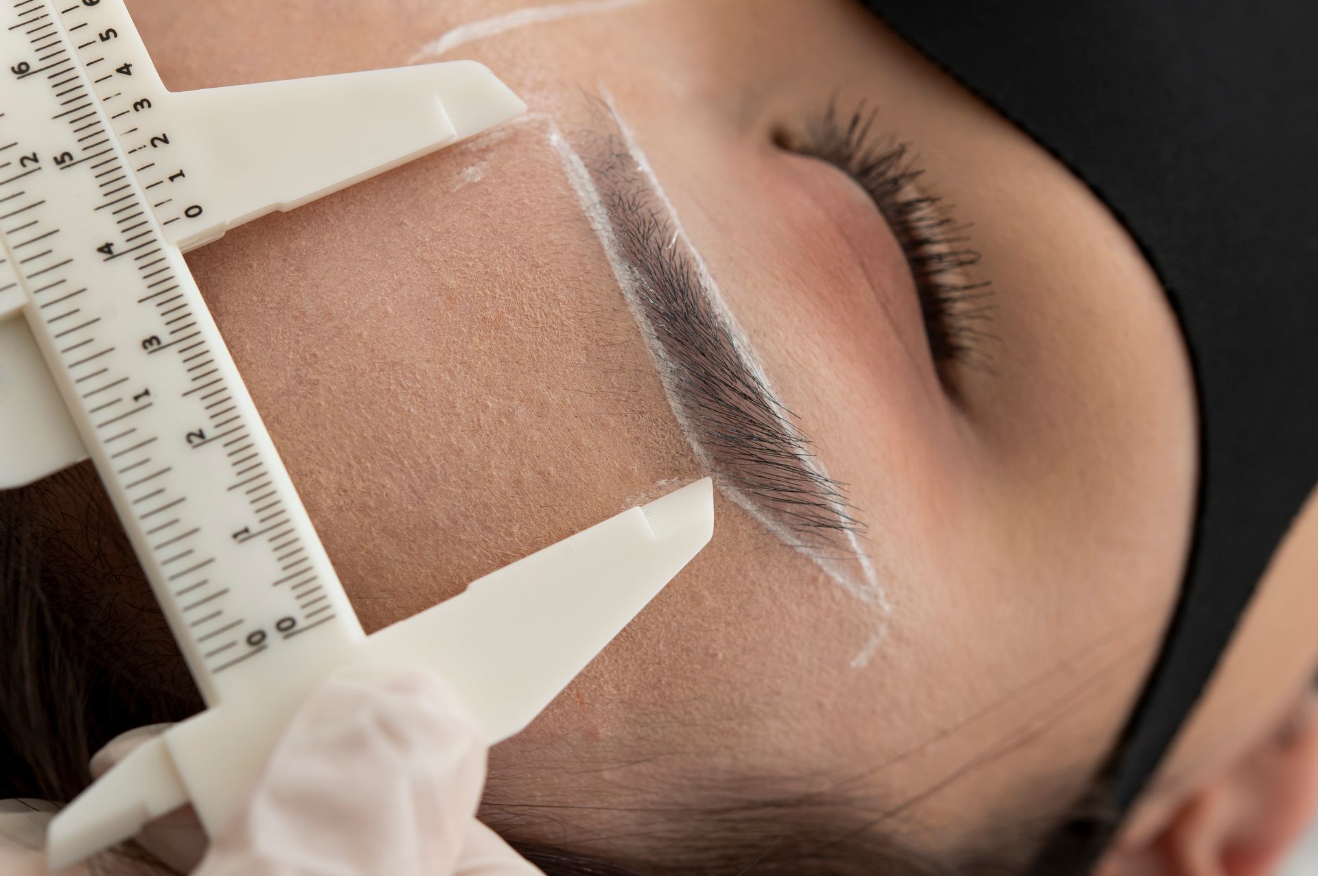 A woman is measuring her eyebrows with a ruler.