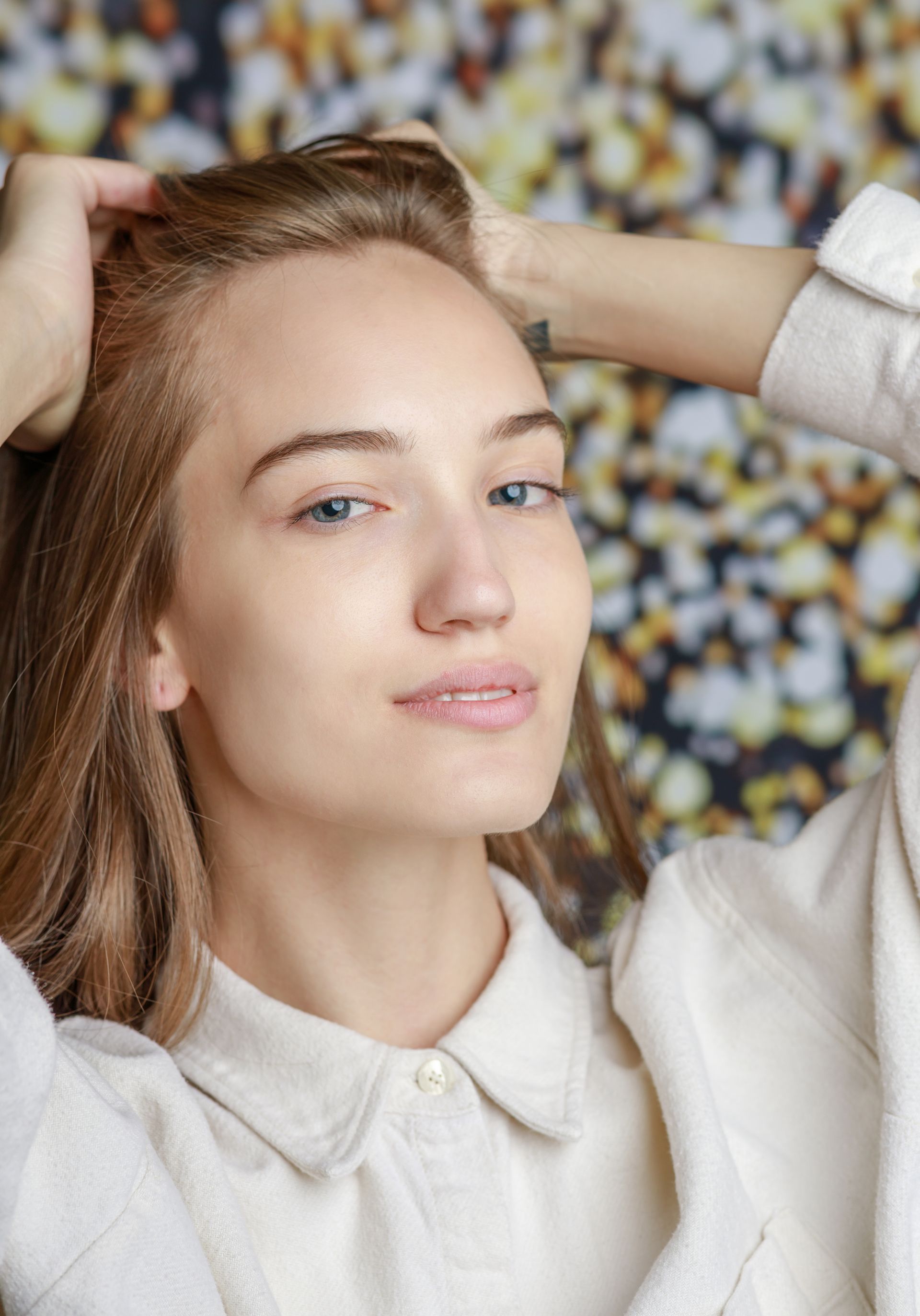 A woman in a white shirt is touching her hair.