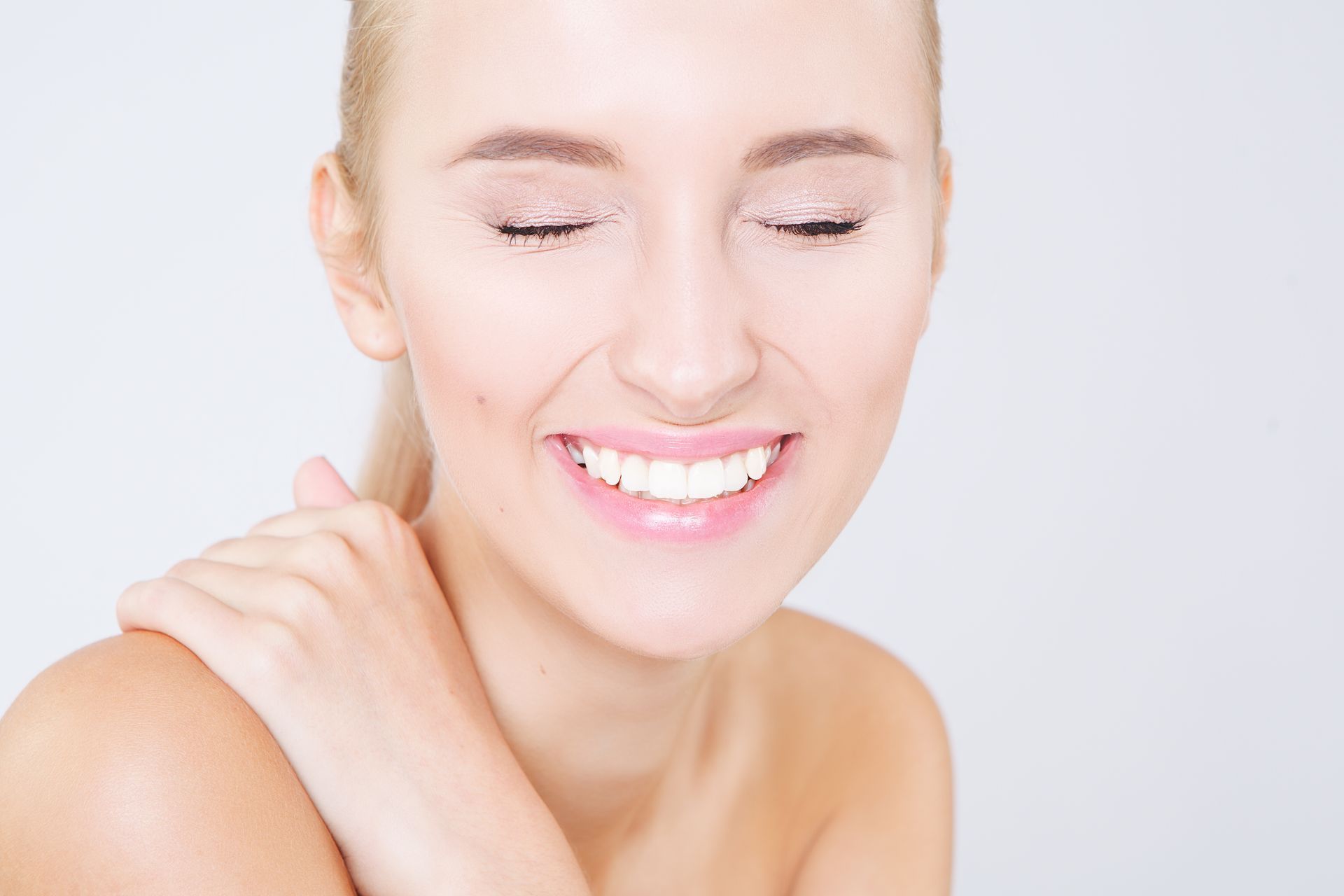 A woman is smiling with her eyes closed and her hand on her shoulder.